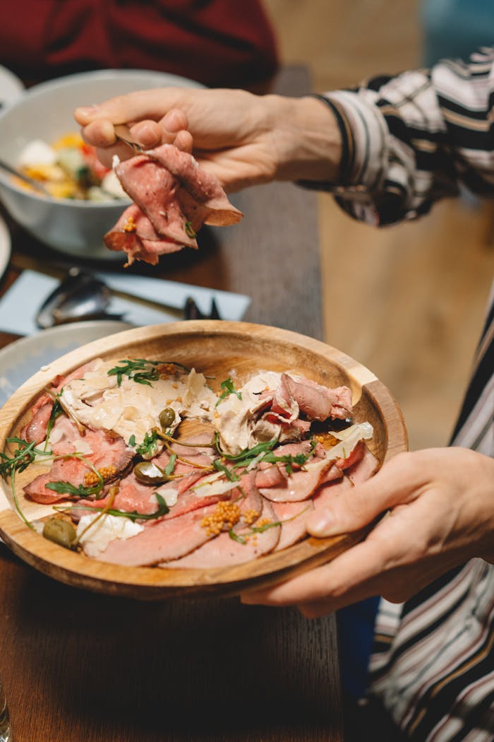 A close-up of sliced meat garnished with herbs, served on a wooden tray.
